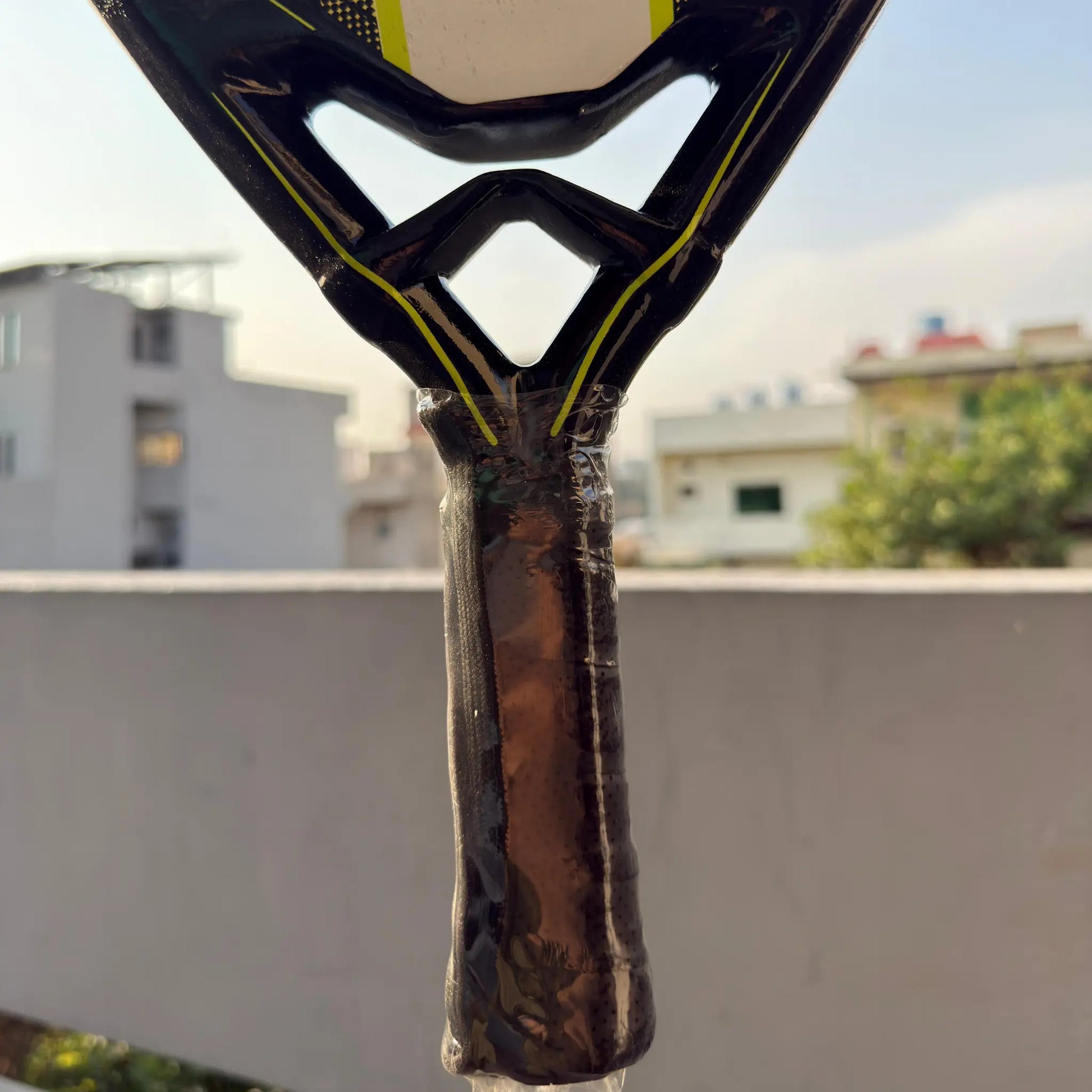 the four degree Close-up of a padel racket handle with a blurred cityscap background